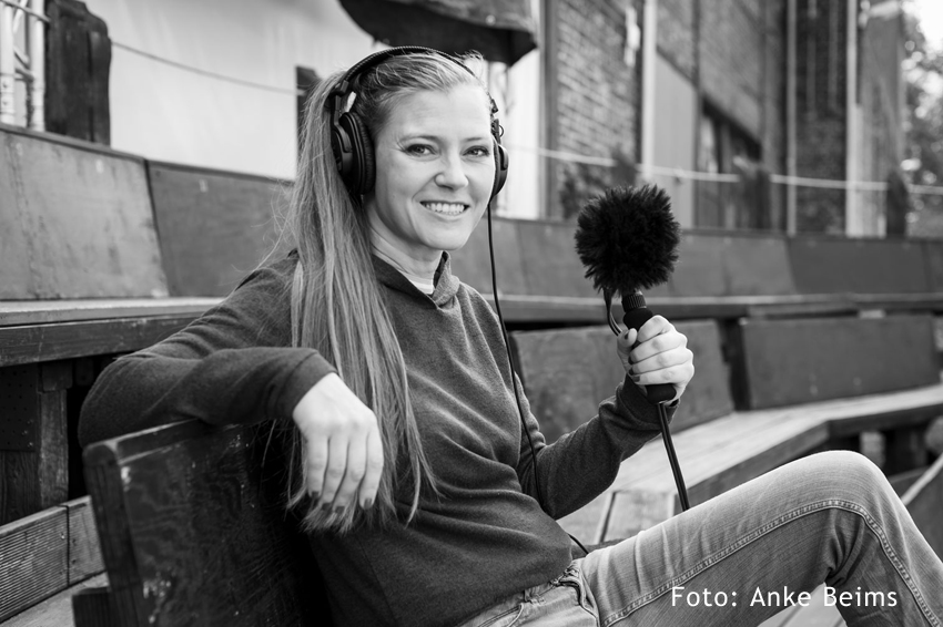 Foto: Porträt von Susanne Franzmeyer mit Mikrofon auf Bankreihe in einem Amphitheater